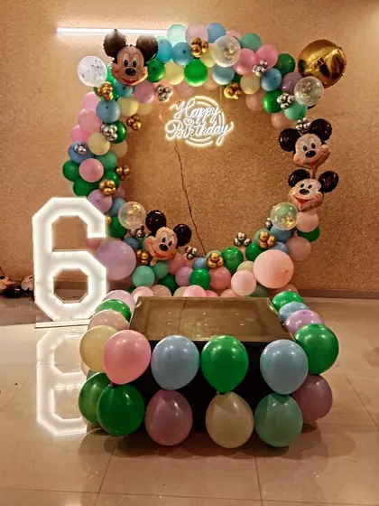 A classic Mickey Mouse themed 6th birthday celebration. The setup features a circular balloon arch with Mickey Mouse ear balloons, a neon 'Happy Birthday' sign, and a large light-up number '6'.