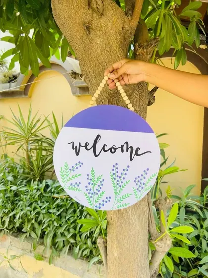 Another look at our 'Welcome' wooden sign, hanging on a tree. The simple yet elegant design with hand-doodled lavender flowers makes for a charming and personal touch to your home's entrance.