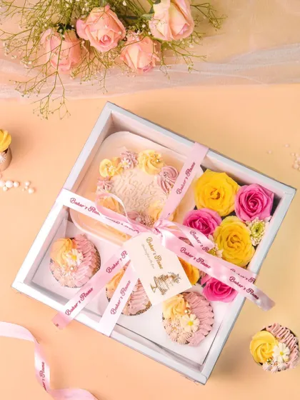 The pink and yellow bakery hamper, beautifully tied with a ribbon. The soft, warm lighting enhances the appeal of the delicious treats and flowers inside.