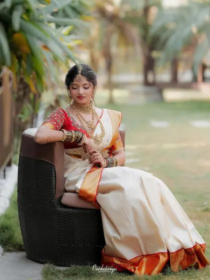 The bride seated in a moment of quiet grace. This full-length portrait showcases her entire bridal look, from the saree to the intricate jewelry.