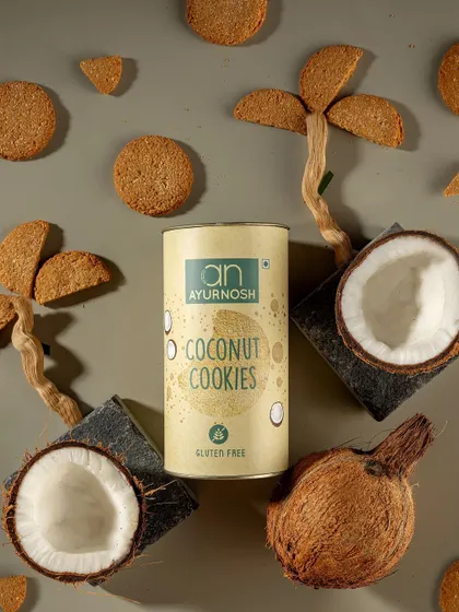 A creative flatlay for Ayurnosh's gluten-free coconut cookies. The ingredients like coconuts and cookie-made palm trees visually tell the story of the product's flavor and natural origins.