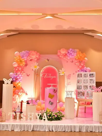 This butterfly-themed first birthday was designed to be absolutely beautiful. The stage features large butterfly wing props, a personalized name panel, and a mix of pink and orange balloons.