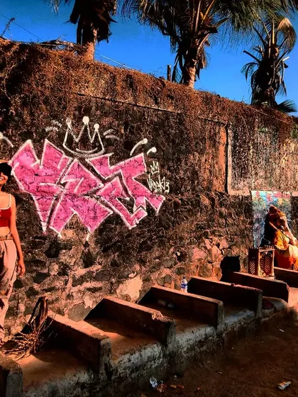 Me striking a pose next to my pink graffiti piece on a rustic wall at Versova beach. The salt, sand, and chaos of the city are the perfect backdrop for street art.