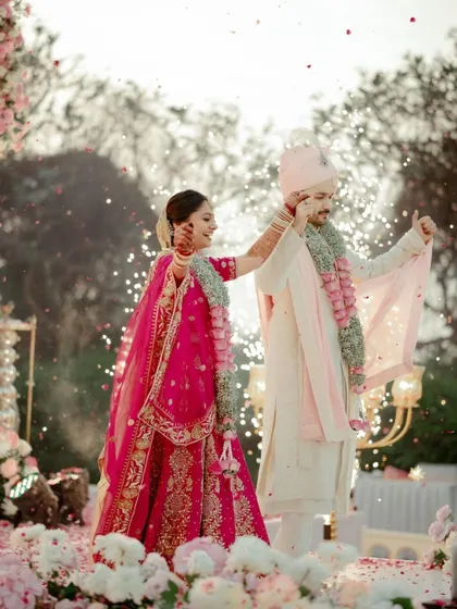 A playful moment during the Varmala ceremony, with the couple sharing a laugh as flower petals are showered upon them. It captures the fun and joy of the wedding rituals.