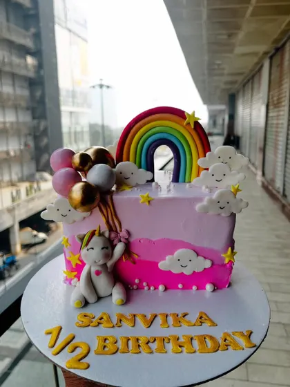 A cheerful half-birthday cake with a unicorn and rainbow theme. This pink rectangular cake is perfect for celebrating the six-month milestone with a touch of magic.