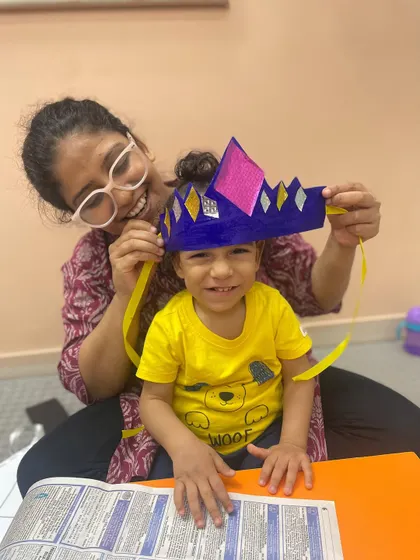 A smiling mother helps her son wear a paper crown they made, a proud and happy moment.