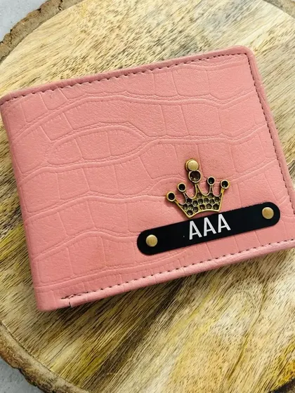 A pink croc-textured wallet with a black name strip and a crown charm. The color contrast makes the personalization pop.