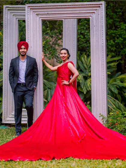 A full-length shot showcasing the impressive train of the red gown. The couple poses with the giant frame props for a modern and stylish pre-wedding photo.