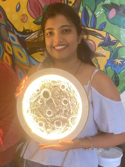 A participant smiles brightly, holding her completed 3D moon lamp against our colourful cafe mural.