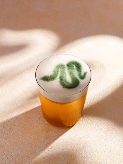 A close-up of a Yautcha cocktail with snake latte art, tying into their "Year of the Snake" theme. This detail shot highlights the creativity of their menu.
