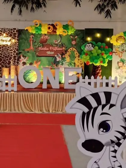 A full-stage view of a jungle safari first birthday. The design includes a lush backdrop, a variety of animal cutouts like a zebra and giraffe, and a large "ONE" sign for the perfect photo opportunity.