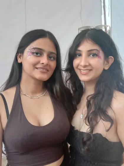 Friends showing off their matching glitter eye makeup. One has a pink glitter wing and the other a more scattered glitter look.