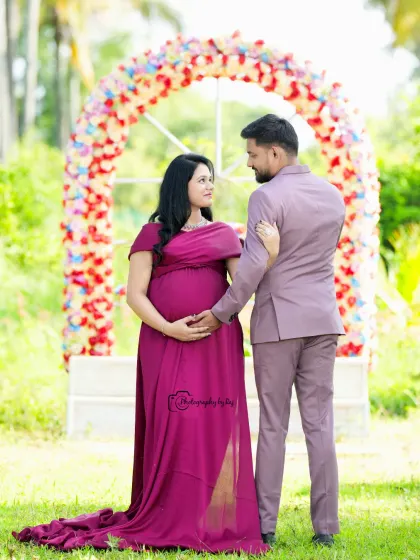 A classic couple's portrait in front of a floral arch. The mother-to-be is wearing a wine-colored gown.