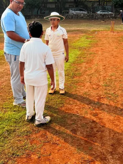 A coach provides personalized feedback to a young batsman on the pitch. This one on one instruction helps players understand and correct their technique in real-time.