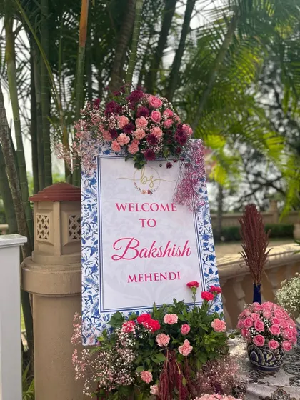 A personalized welcome sign for the "Bakshish Mehendi," framed with an abundance of pink and purple flowers, setting a celebratory tone.
