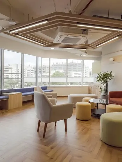 A large, sunlit lounge with expansive windows offering city views. The space is furnished with comfortable sofas and ottomans in warm and cool tones, creating a perfect setting for team-wide gatherings or quiet relaxation.