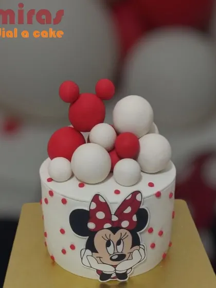 A classic Minnie Mouse cake with a modern twist. The design features Minnie's face on a polka-dotted background, topped with red and white spheres for a fun, bubbly look.