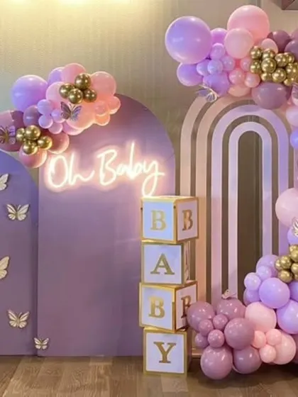 A beautiful "Oh Baby" shower with a purple butterfly theme. This setup includes stacked "BABY" blocks, gold butterfly decals, and a stunning balloon garland in shades of lavender and pink with gold chrome accents.