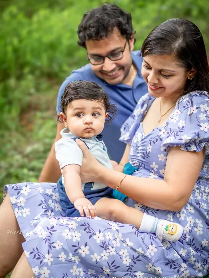 A mother holds her baby while the father looks on with a smile during a relaxed outdoor session. The image captures a quiet, loving family interaction, highlighting the natural and unposed style of my work.
