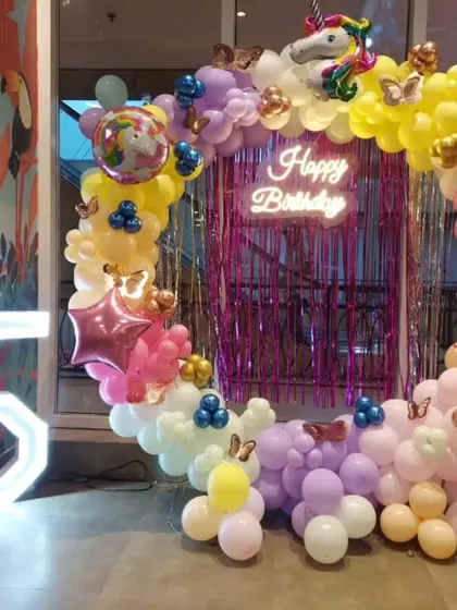 A whimsical unicorn-themed 5th birthday party with a circular balloon arch in pastel colors, a shimmer backdrop, a 'Happy Birthday' neon sign, and a large marquee number '5'.