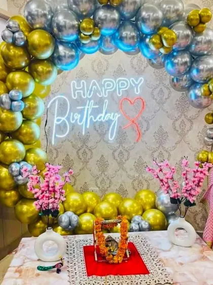 A golden and silver chrome balloon ring creating a festive backdrop for a birthday pooja or celebration at home.