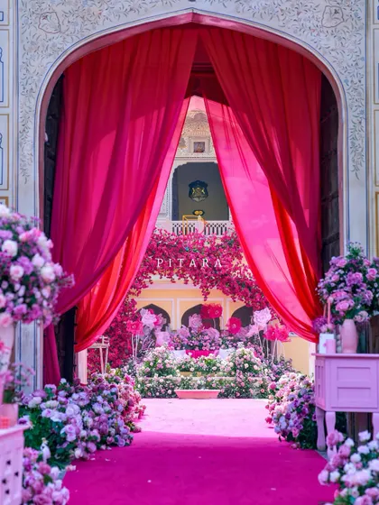 This is how we do royal entrances. A vibrant gulabi carpet and lush floral arrangements guide guests through majestic palace arches, framed by dramatic fuchsia drapes. It’s a welcome that promises the grandeur to come.