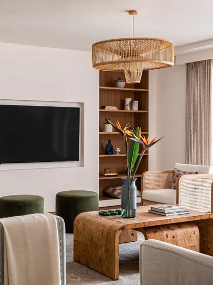 The living room is designed for relaxed, elegant living. A large rattan chandelier is the centerpiece, while comfortable seating and pops of green create a cozy space for the family to gather.