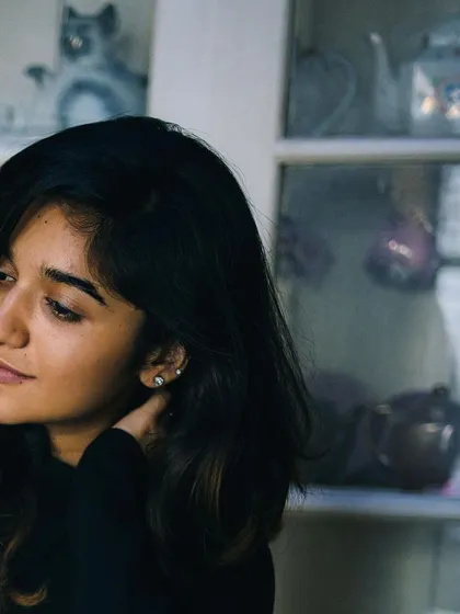A natural light portrait of a woman looking thoughtfully to the side, with a cabinet of curios in the background. The setting adds a touch of personality and story to this simple, beautiful shot.