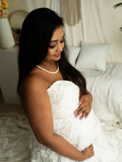 A close-up shot focusing on the connection between mother and bump. The intricate texture of the white lace gown adds a beautiful detail.