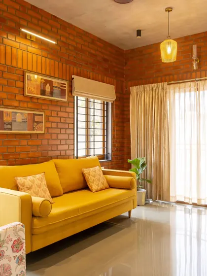 A duplicate image of the yellow sofa against the brick wall in the Akshaynagar duplex.