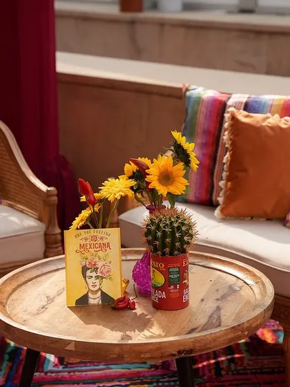 A close-up of a seating area, showing the Frida Kahlo cushions and a tabletop decorated with sunflowers and a cactus.