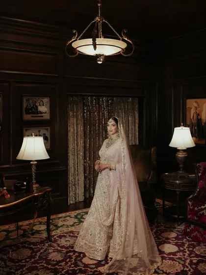 A full-length portrait of Sanskriti at Rambagh Palace. The dark, moody interior adds a sense of drama and old-world luxury to her shimmering lehenga.