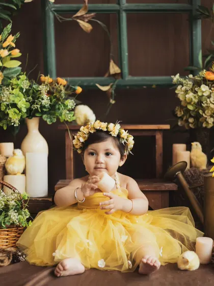 A little ray of sunshine in our sunflower garden setup. The bright yellow dress and floral crown make for a cheerful and vibrant baby portrait.