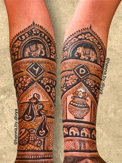Another detailed shot of a bridal forearm design. This piece includes the couple's initials, a kalash, and birds carrying auspicious symbols, all rendered in a bold, clean style.