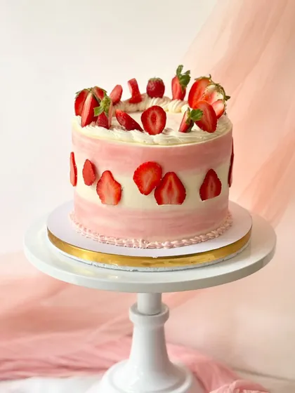 A stunning strawberry cake with pink and white striped buttercream. The cake is decorated with sliced strawberries around the base and topped with a pile of fresh fruit.