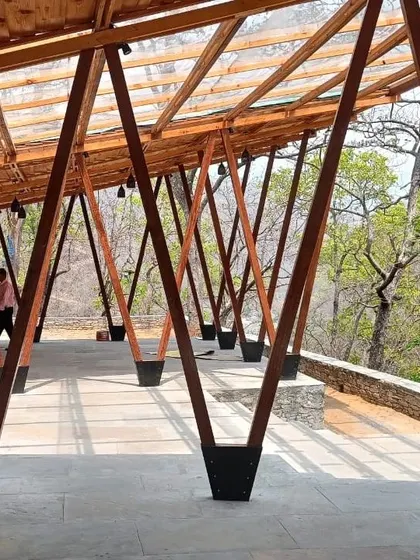**Angling Centre, Pancheshwar:** A person walking through the pavilion gives a sense of the scale and the immersive experience of being under the complex wooden roof structure, surrounded by the dramatic landscape.