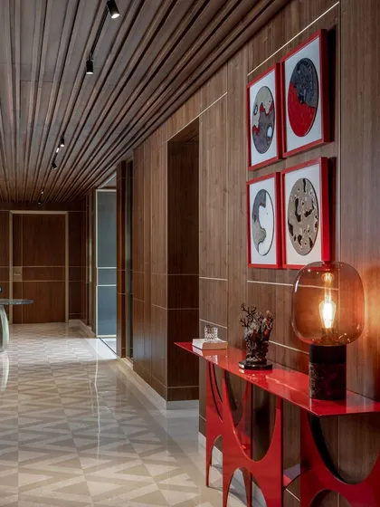 A long corridor lined with wood panels and accented by a vibrant red console table. We use art and statement furniture to turn transitional spaces like hallways into memorable design moments.