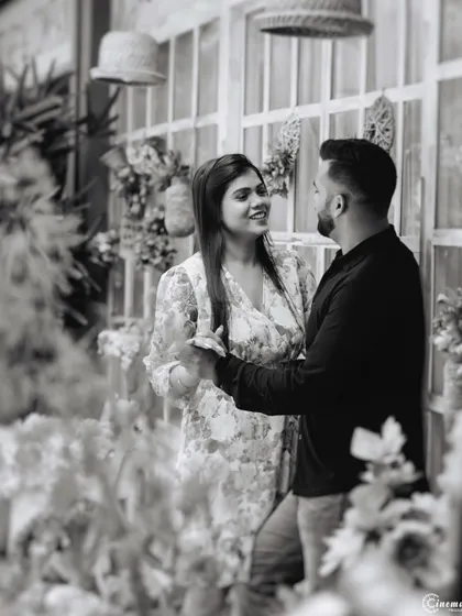 A black and white shot of a couple sharing a dance-like pose in a beautifully decorated setting. The monochrome effect adds a timeless, classic feel to this romantic interaction.