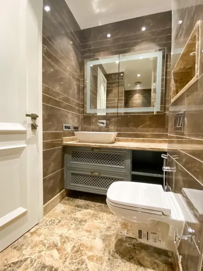 Another one of our spa-like bathrooms at C-926, this one featuring a distressed-finish vanity, a large backlit mirror, and beautiful brown marble tiles.