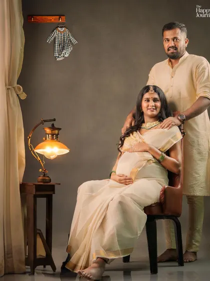 This image showcases the complete scene, with the couple framed by soft curtains and warm light, creating a cozy and intimate atmosphere for their traditional maternity photoshoot.