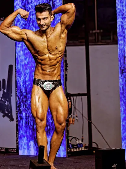 A classic physique pose on stage. This pose is designed to showcase symmetry, muscle mass, and overall aesthetics, key elements of my body transformation coaching.
