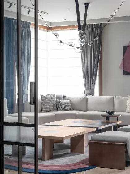 A glimpse into the living room through a sleek, glass-paneled sliding door. This view highlights the open, airy feel of the space, with a focus on modern furniture and a cohesive color palette.
