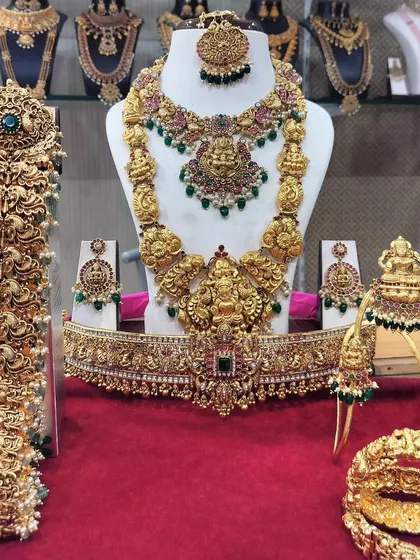 A complete South Indian bridal set, ready for a grand wedding. This gold-look alike set includes a Lakshmi choker, a long haram, matching jhumkas, a vaddanam (waist belt), vanki (armlets), and a full bridal hair accessory set (jadai).