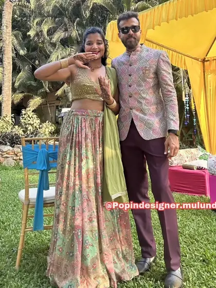 A happy couple at what looks like a mehendi or haldi function. The groom is wearing a stylish printed Jodhpuri-style jacket with maroon trousers, a great Indo-Western choice.