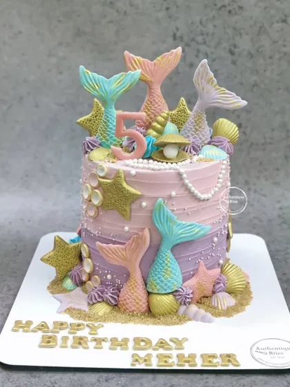 A magical mermaid cake with multi-colored tails and golden stars. The pink and purple ombre frosting adds to the enchanting look.