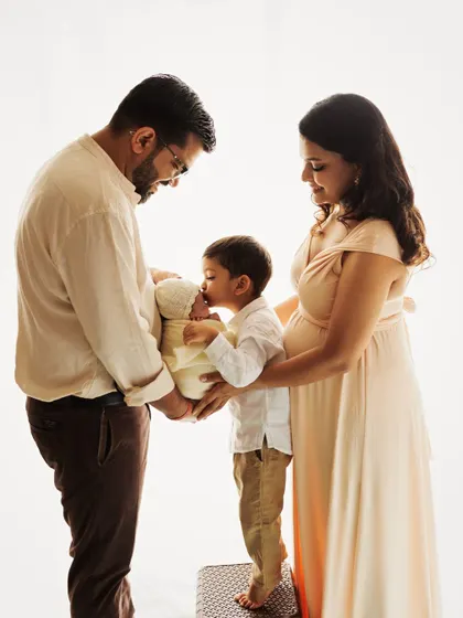 The family is complete. A big brother gives his new sibling a gentle kiss in this heartwarming family portrait, capturing a beautiful moment of growing love.