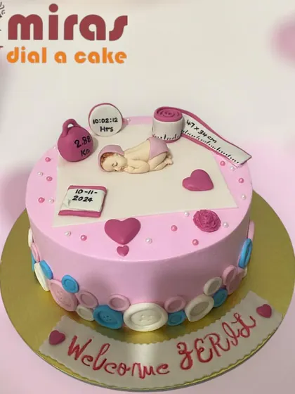 A heartwarming "Welcome Home" cake for a new baby. This pink cake is decorated with buttons and hearts and features a figurine of the baby with details like weight and time of birth.