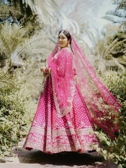 A stunning full-length portrait of the bride in her bright pink Anand Karaj lehenga. The flowing dupatta and the lush green background make for a vibrant and beautiful shot.