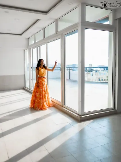 A bride in her vibrant Haldi outfit, standing in a sunlit room. The long shadows and bright light create a modern and architectural feel, beautifully contrasting with her traditional attire.