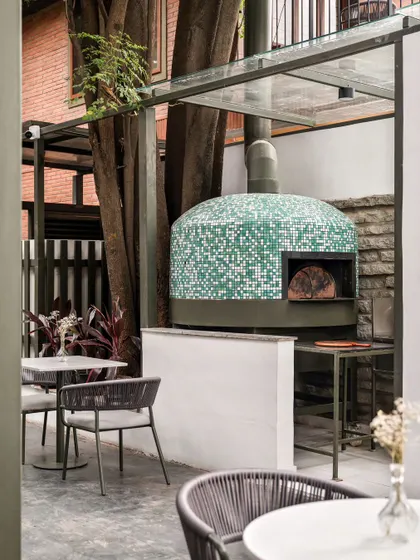A traditional pizza oven clad in green and white mosaic chips stands as a playful focal point at Kana Cafe. This feature adds a unique, artisanal touch to the outdoor dining experience.